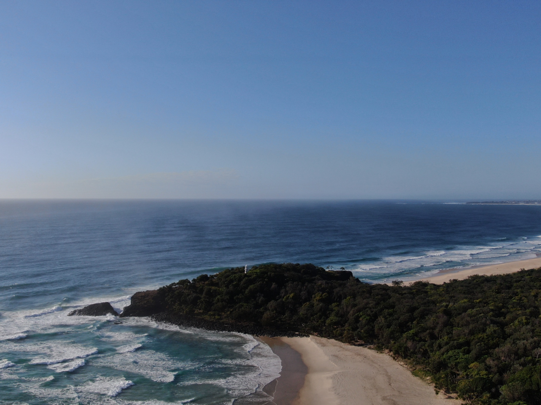 Aerial view of a coastal headland with deep blue ocean under a clear sky